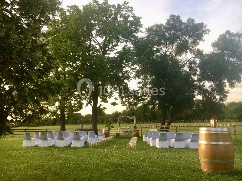 Chaises blanches disposées en extérieur autour d'une arche décorée, sur une pelouse entourée d'arbres.