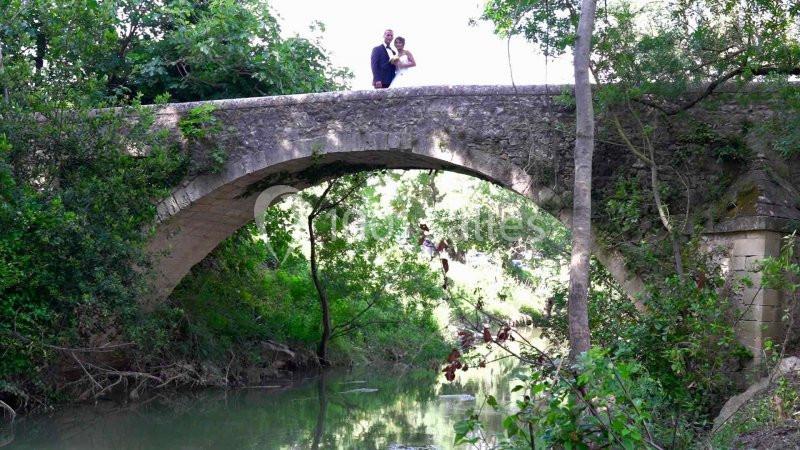 Un couple debout sur un pont en pierre au-dessus d'une rivière entourée de végétation.