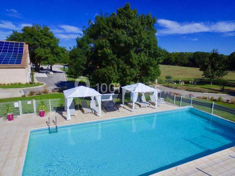 Piscine extérieure avec transats sous des tonnelles blanches, entourée de verdure et d'un bâtiment avec panneaux solaires.