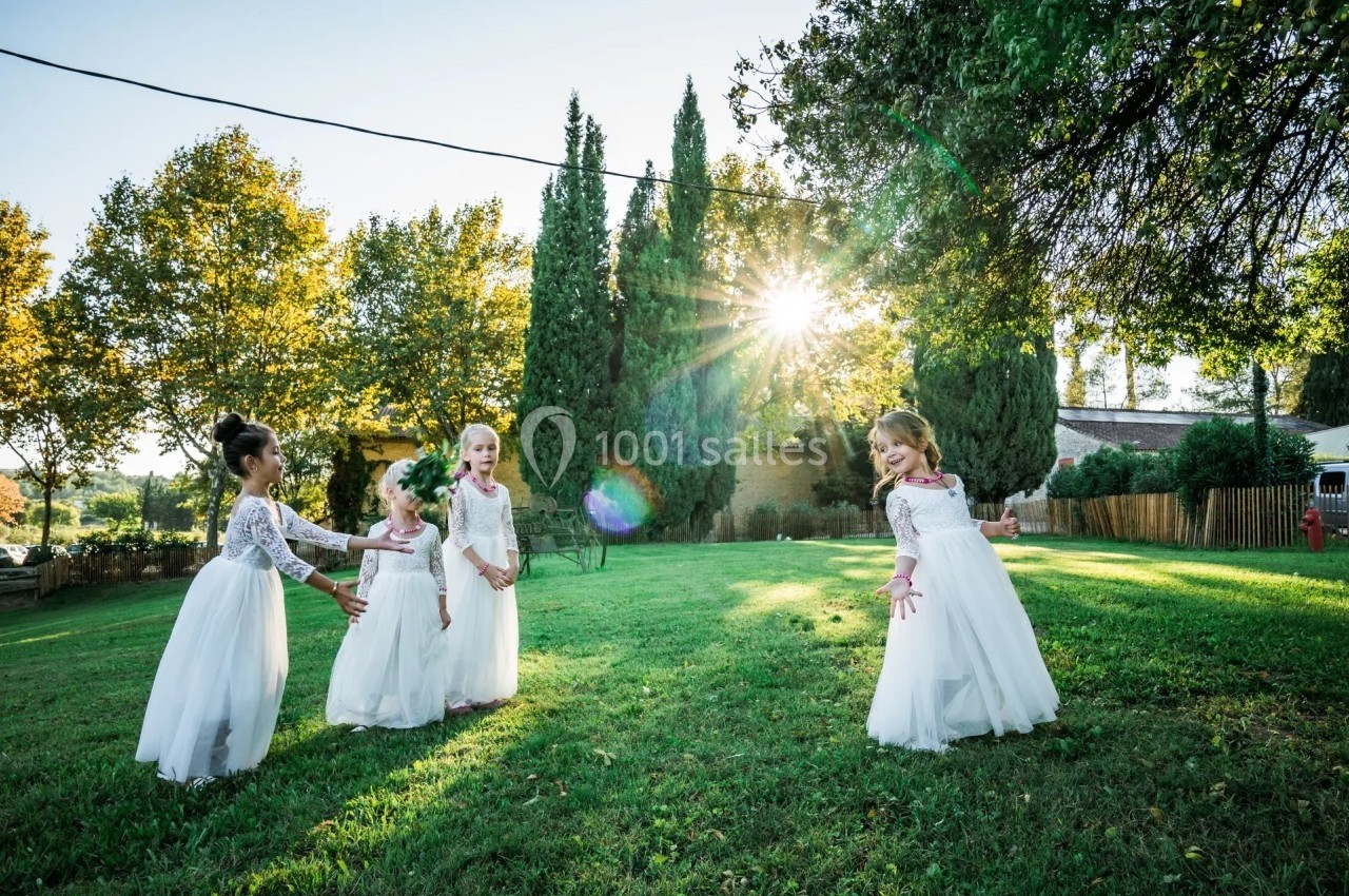 Quatre jeunes filles en robes blanches jouent dans un jardin verdoyant sous un soleil éclatant.