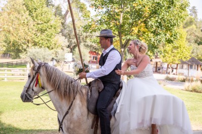 Miniature Location salle Le Crès (Hérault) - Domaine du Mas du Pont #25 Un couple en tenue de mariage pose devant un groupe de cavaliers alignés sur des chevaux dans un espace verdoyant.