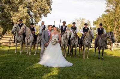Miniature Location salle Le Crès (Hérault) - Domaine du Mas du Pont #29 Un couple en tenue de mariage pose devant un groupe de cavaliers alignés sur des chevaux dans un espace verdoyant.