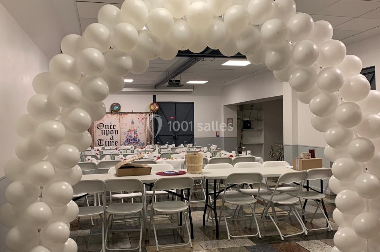 Arche de ballons blancs décorant une salle avec tables et chaises alignées pour un événement festif.