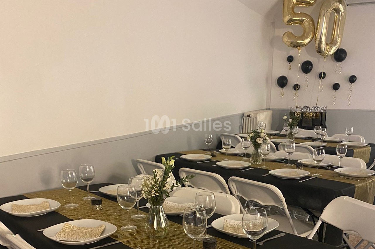 Salle décorée pour un 50e anniversaire avec tables dressées, nappes dorées et ballons dorés et noirs.