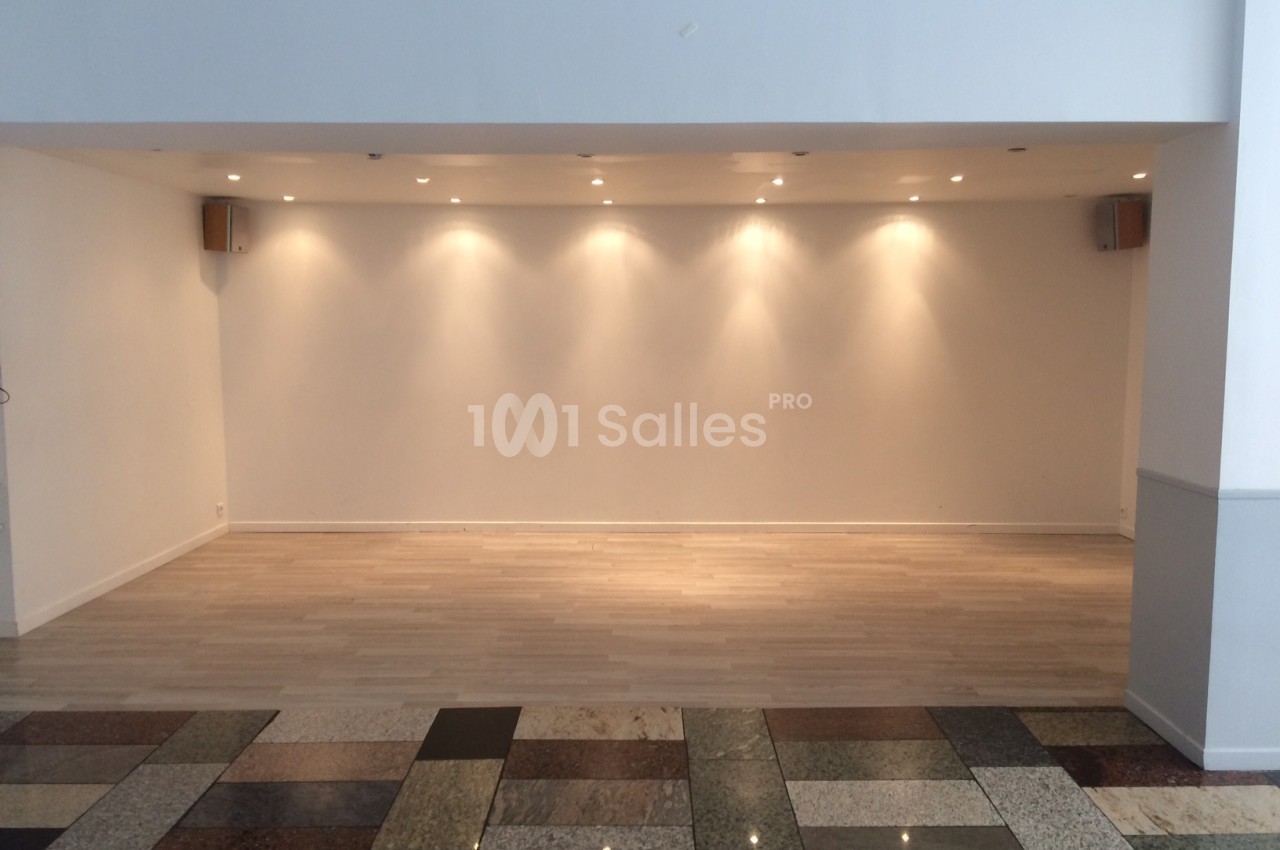 Salle vide avec parquet clair, murs blancs, éclairage encastré au plafond et sol en carrelage multicolore au premier plan.