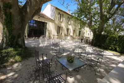 Miniature Location salle Avignon (Vaucluse) - Domaine de Rochegude #9 Façade d'une maison provençale avec terrasse ombragée, tables en fer forgé et grand arbre au premier plan.
