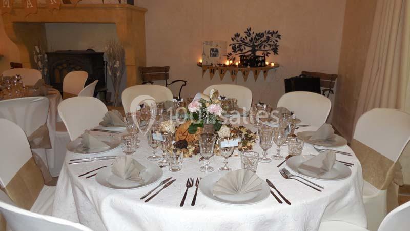 Table ronde élégamment dressée avec nappes blanches, serviettes pliées, verres et centre de table floral.