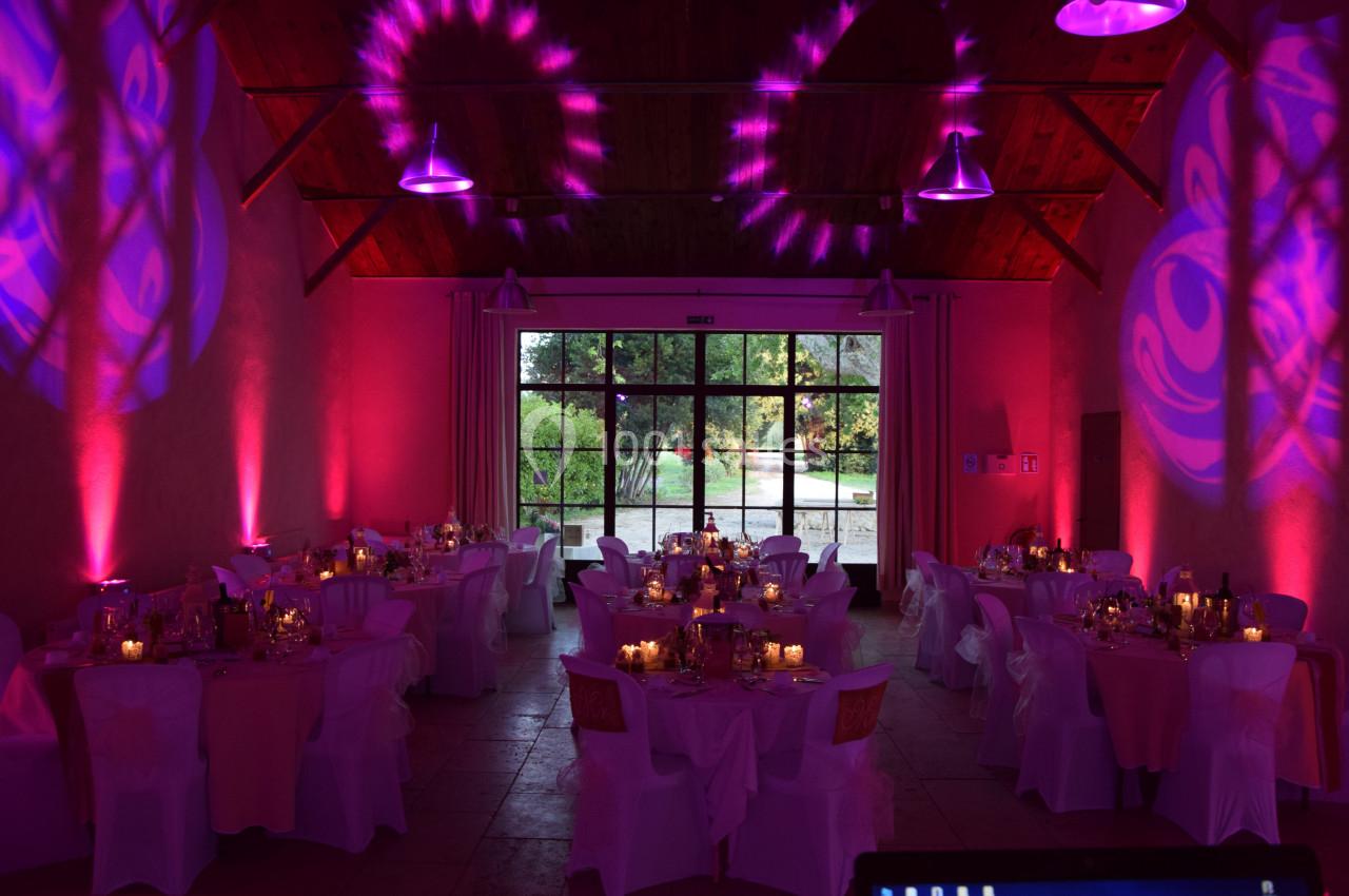 Salle de réception décorée avec des tables dressées, éclairage rose et violet, et vue sur un jardin à travers de grandes…