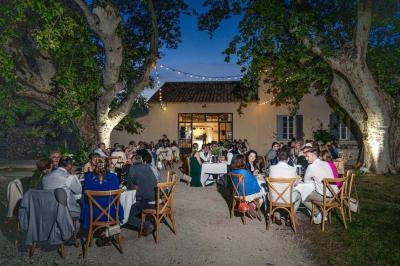 Miniature Location salle Avignon (Vaucluse) - Domaine de Rochegude #5 Façade d'une maison provençale avec terrasse ombragée, tables en fer forgé et grand arbre au premier plan.