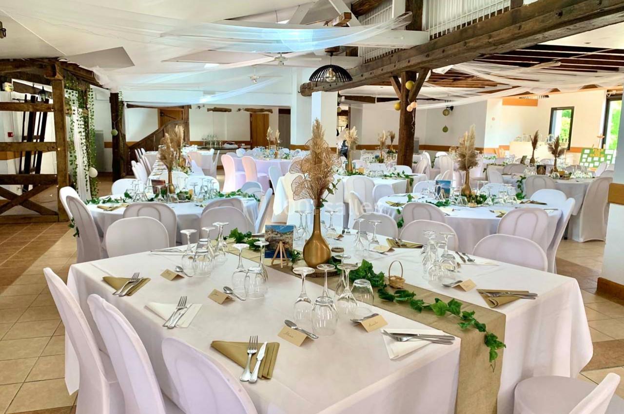 Salle de réception décorée avec des tables dressées, nappes blanches, chaises assorties et ornements végétaux.