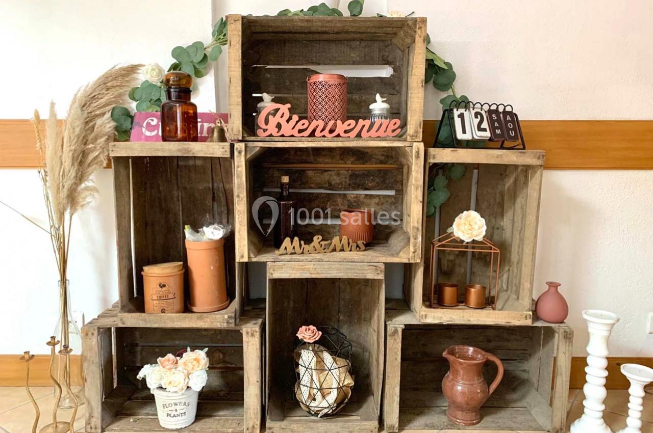 Décoration composée de caisses en bois empilées, contenant des objets variés, fleurs et éléments rustiques.