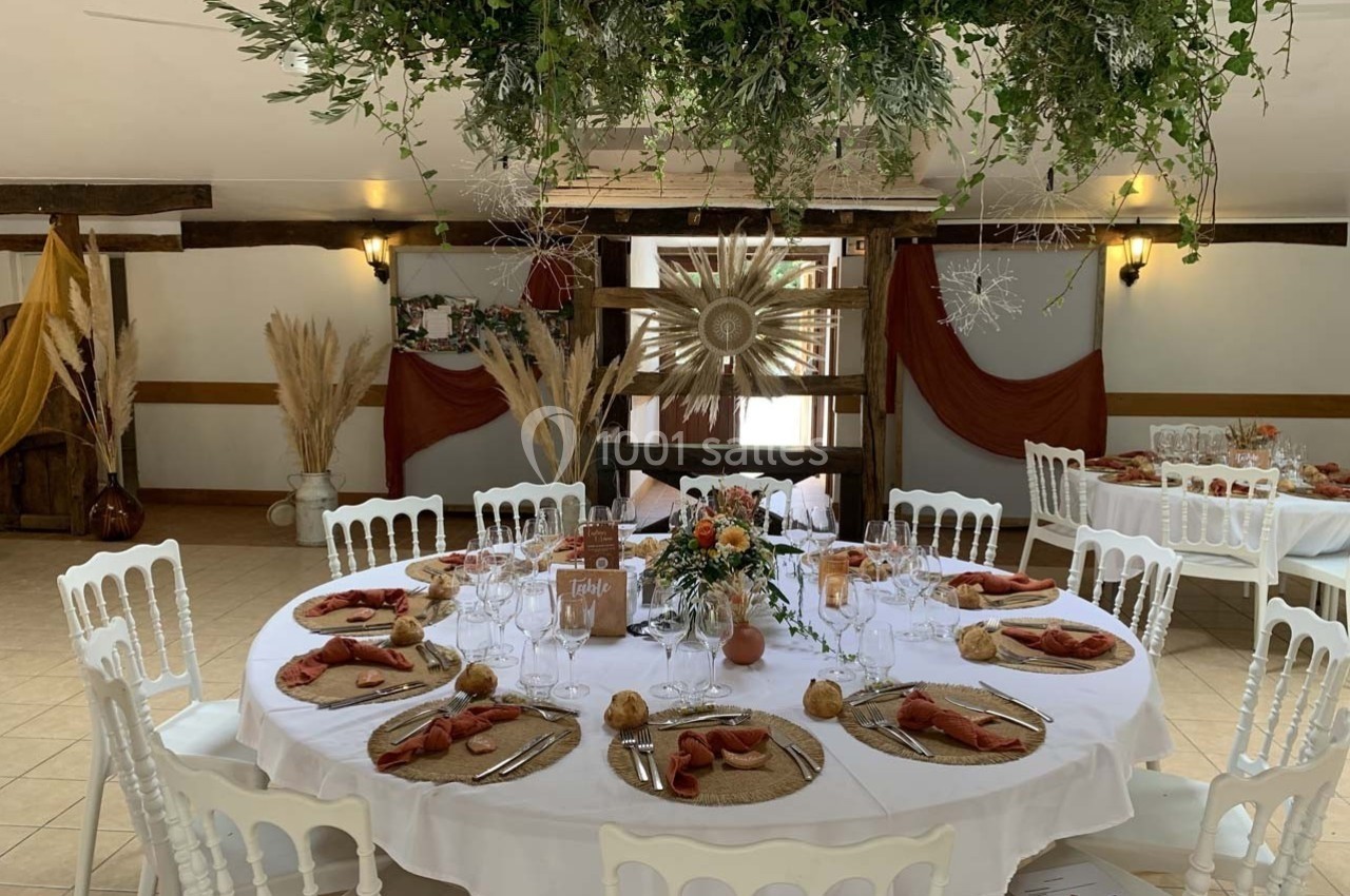 Table ronde décorée pour un événement, avec nappes blanches, serviettes orange, vaisselle élégante et centre de table floral.