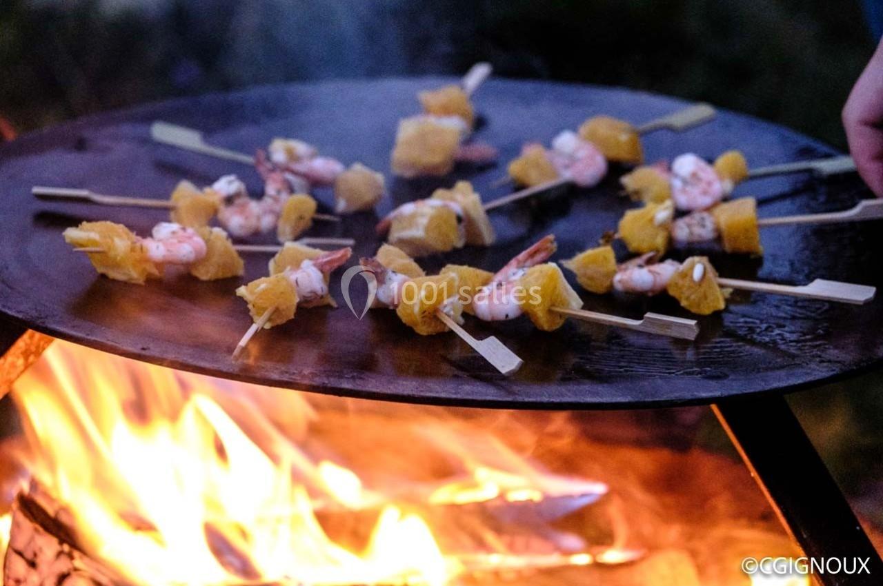 Brochettes de crevettes et morceaux d'ananas grillant sur une plancha au-dessus d'un feu de bois.