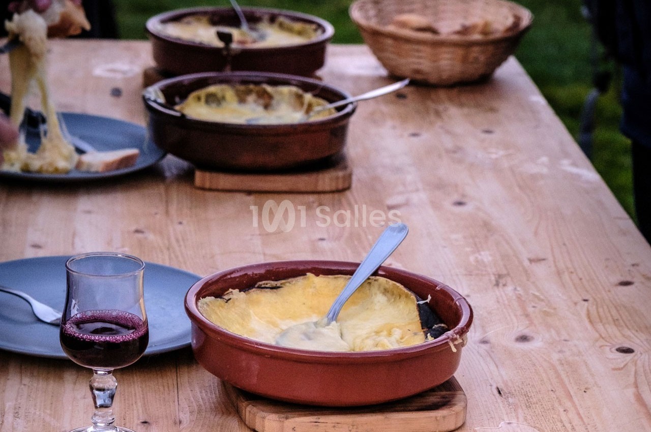 Plat de fromage fondu servi dans des ramequins en terre cuite sur une table en bois, avec du vin rouge et du pain.