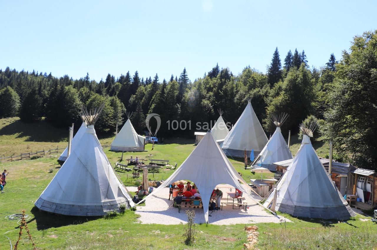 Groupe de tipis installés dans une clairière entourée de forêt, avec des tables et des personnes au centre.