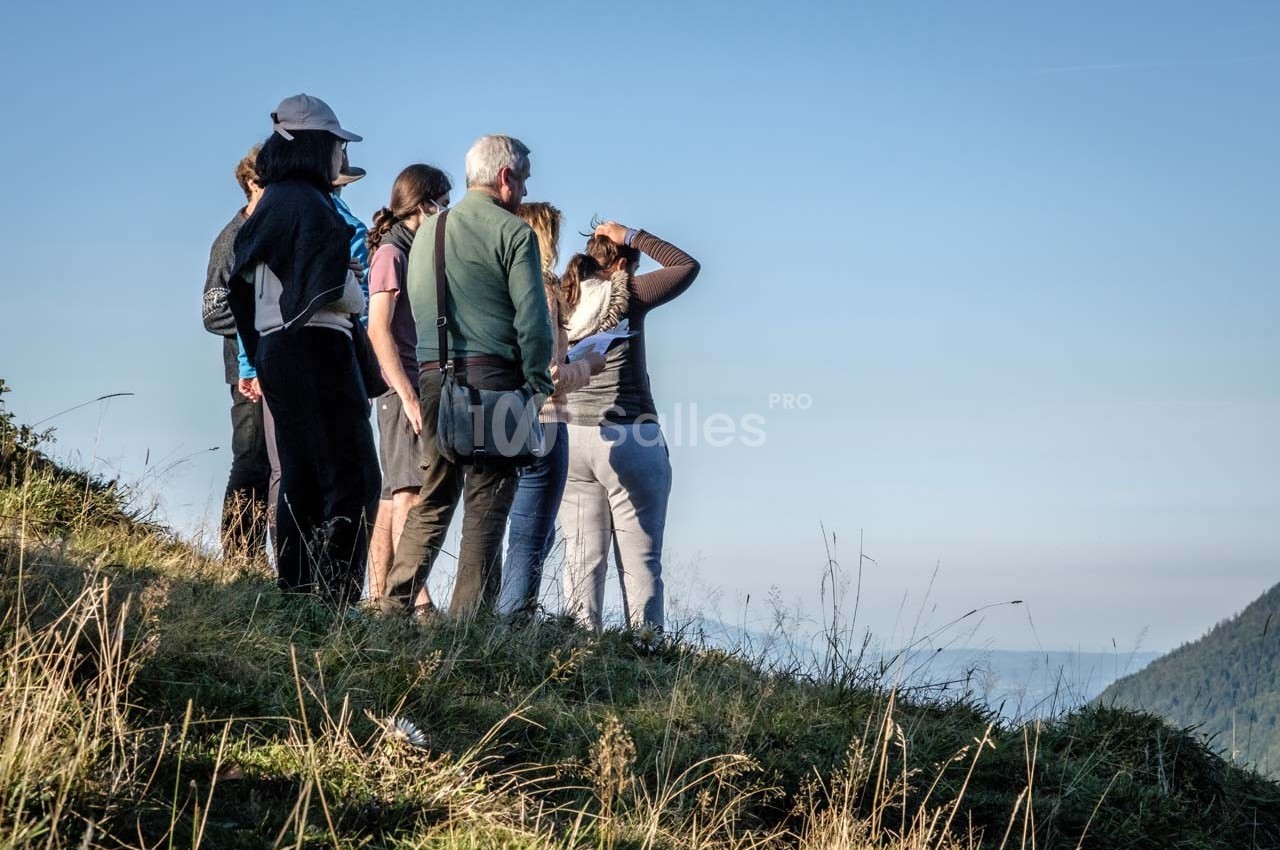 Un groupe de personnes observe un paysage depuis une colline herbeuse par temps clair.