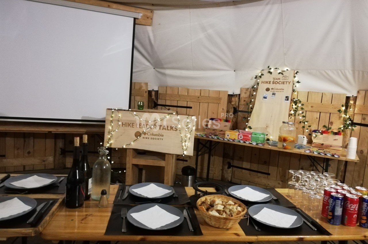 Table dressée avec assiettes et verres devant un écran de projection, décorée pour une présentation ou un événement.