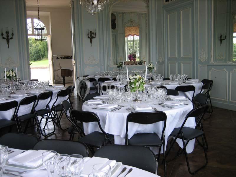 Salle élégante avec tables rondes dressées de nappes blanches, vaisselle raffinée et chaises noires pliantes.