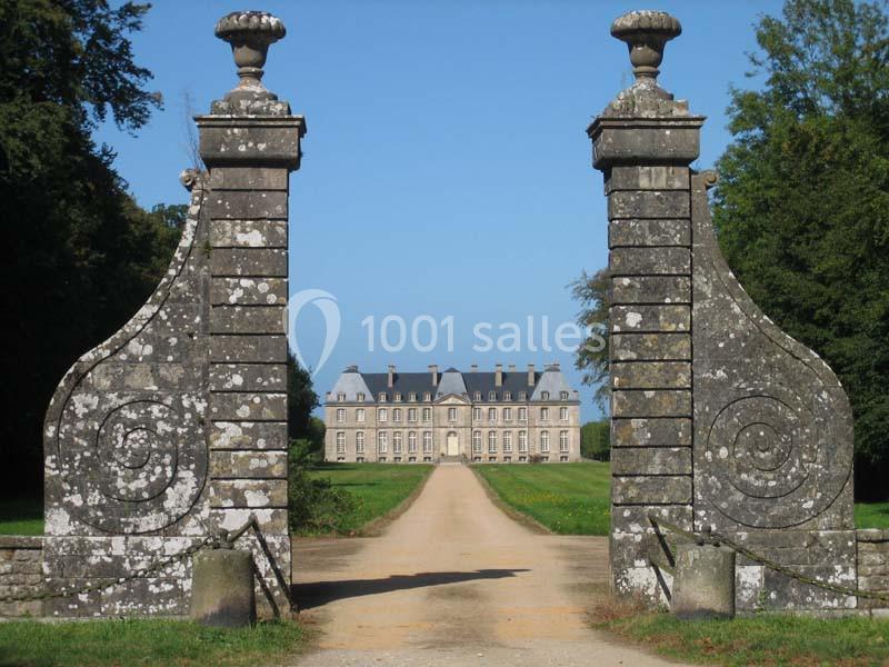 Entrée monumentale en pierre avec un chemin menant à un château au loin, entouré de verdure.