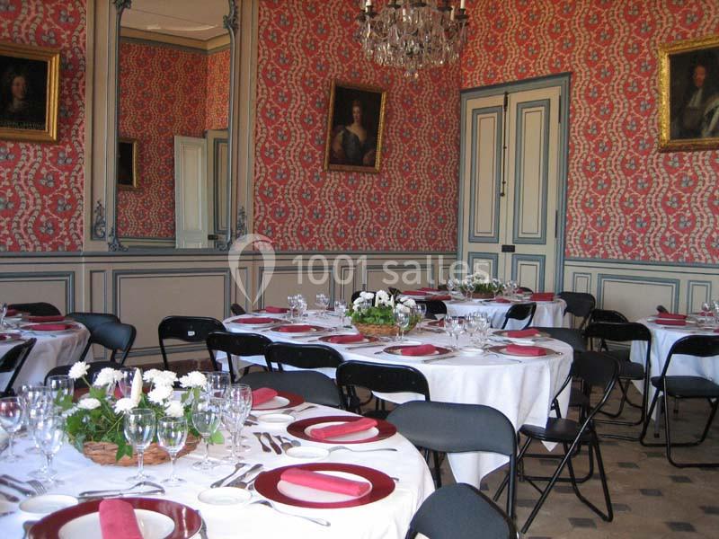 Salle à manger élégante avec tables rondes dressées, nappes blanches, serviettes rouges et décorations florales.