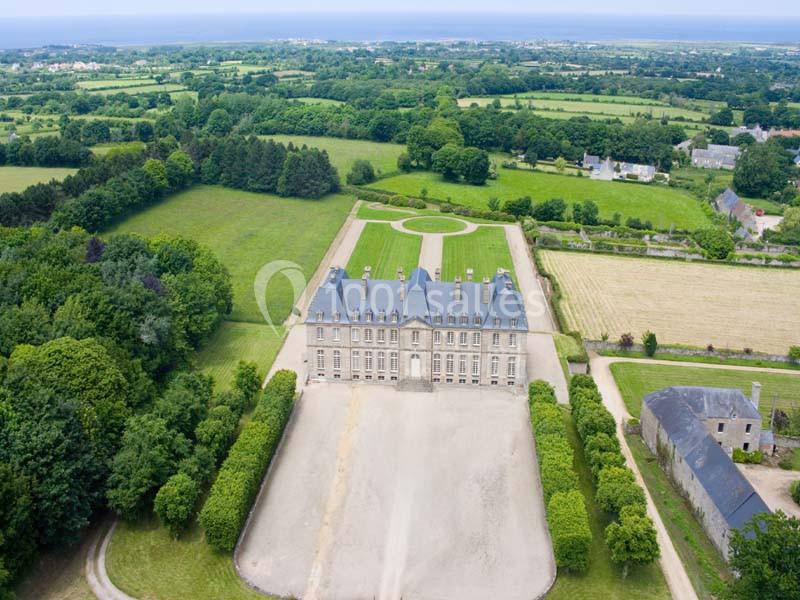 Vue aérienne d'un château entouré de jardins, d'arbres et de champs dans un paysage rural.