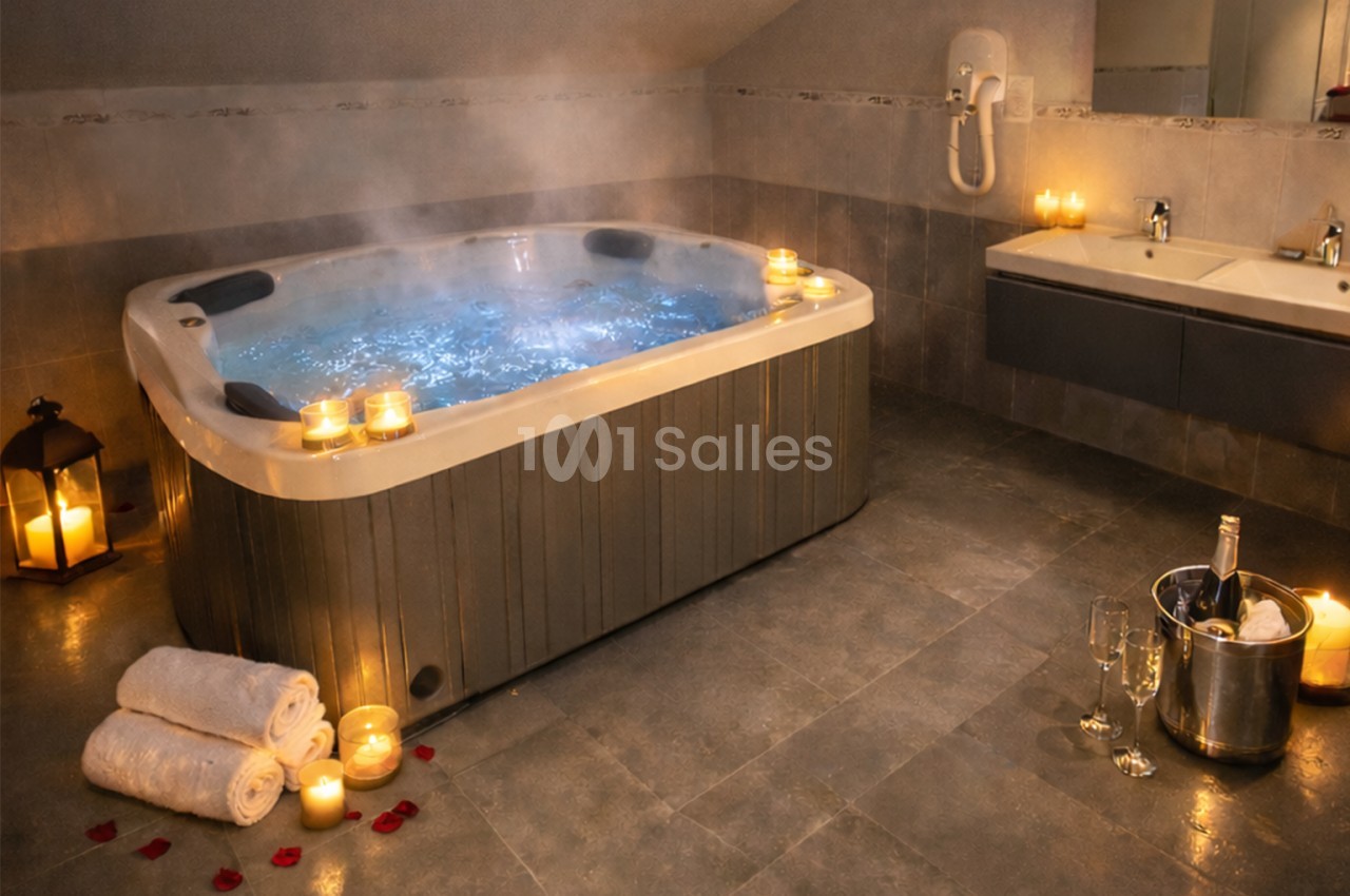 Bain à remous allumé dans une salle de bain tamisée, entouré de bougies, serviettes, pétales de rose et champagne.