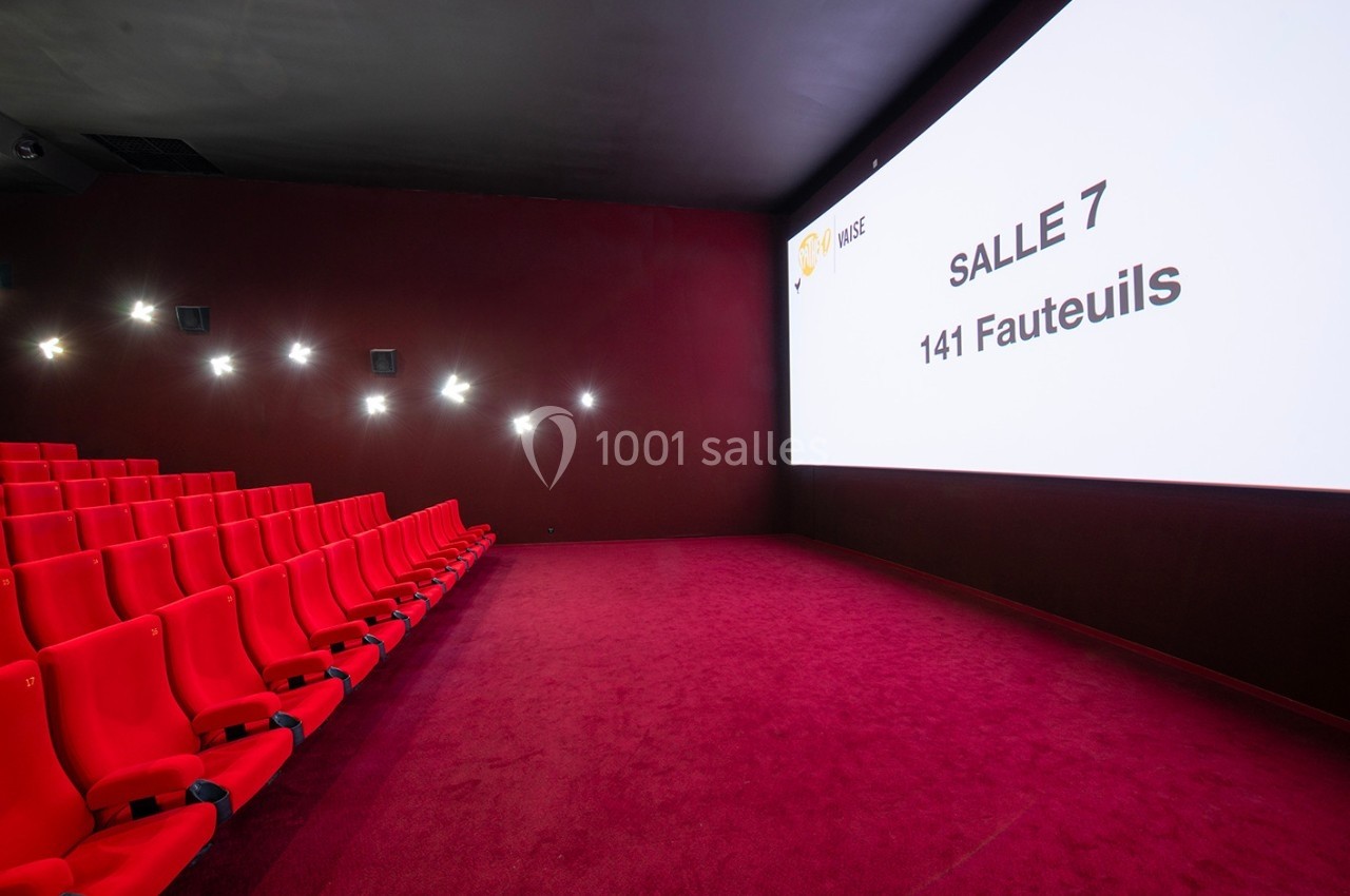 Salle de cinéma vide avec des sièges rouges, un écran affichant ’Salle 7, 141 fauteuils’ et un sol recouvert de moquette…