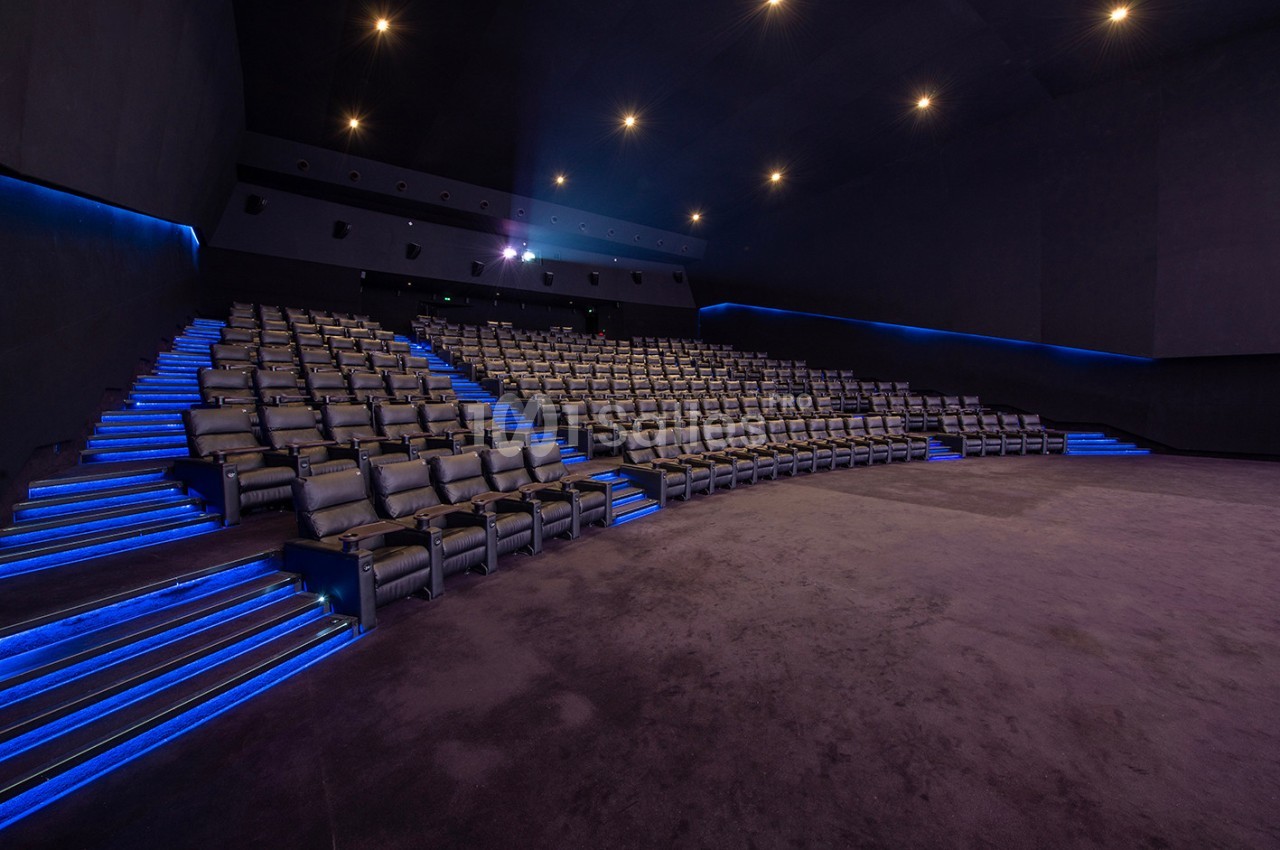 Salle de cinéma vide avec rangées de sièges en cuir et éclairage bleu le long des allées.