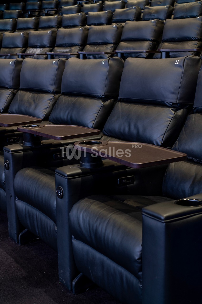 Fauteuils de cinéma en cuir noir avec tablettes et porte-gobelets intégrés, alignés dans une salle vide.