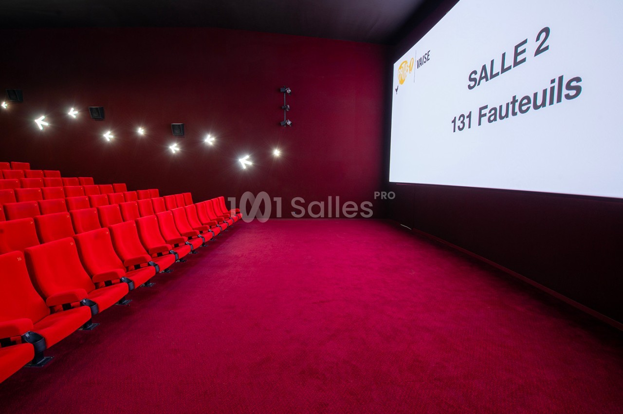 Salle de cinéma avec des sièges rouges alignés et un écran affichant ’Salle 2, 131 fauteuils’ sur un fond rouge.