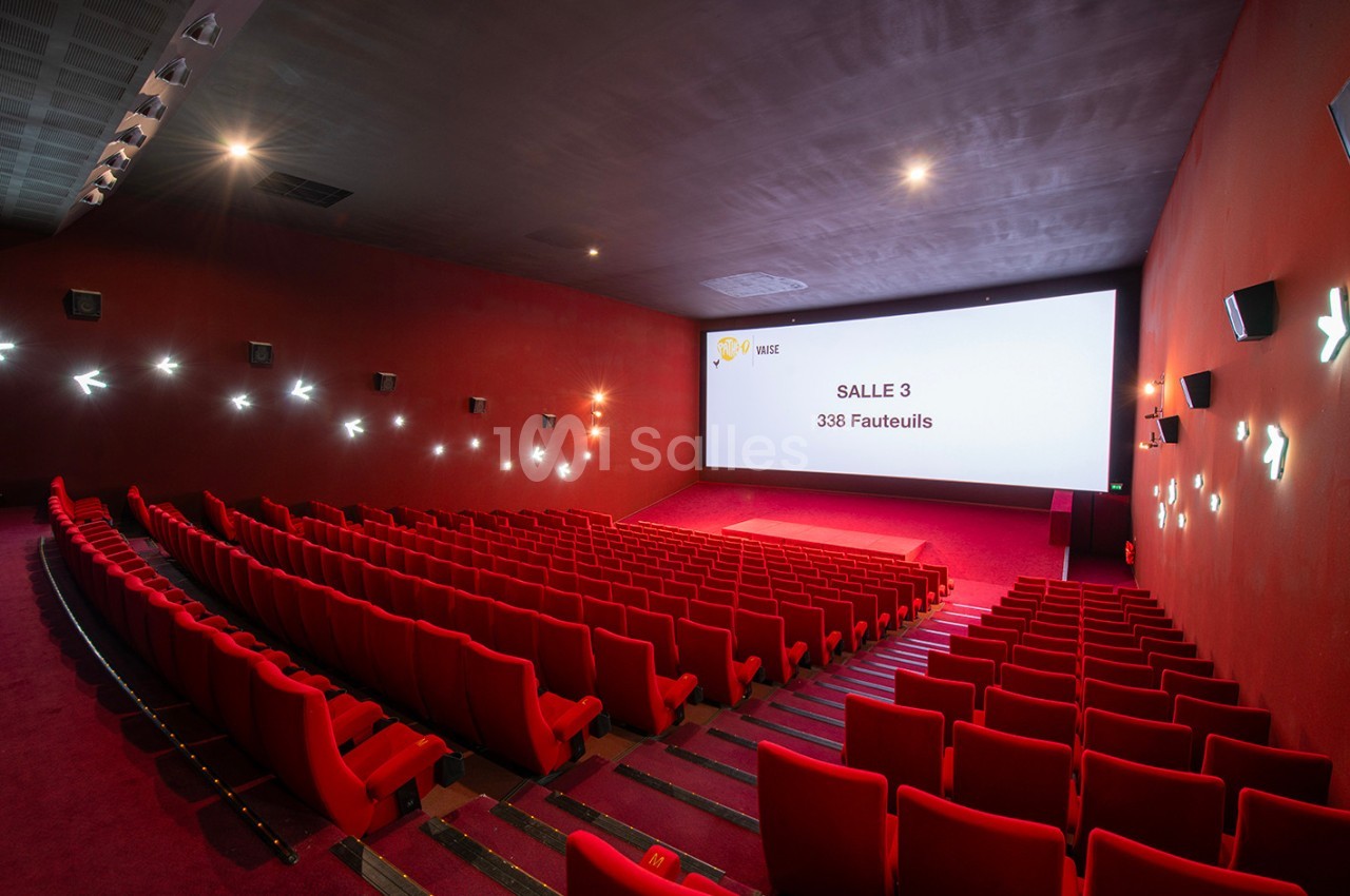 Salle de cinéma vide avec des rangées de fauteuils rouges, écran blanc affichant ’Salle 3 - 338 fauteuils’.