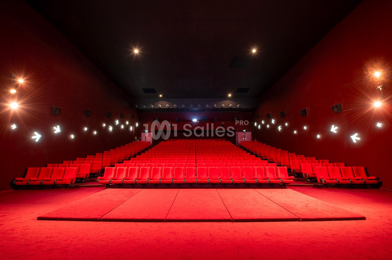 Salle de cinéma vide avec des rangées de sièges rouges et un éclairage tamisé sur les murs.