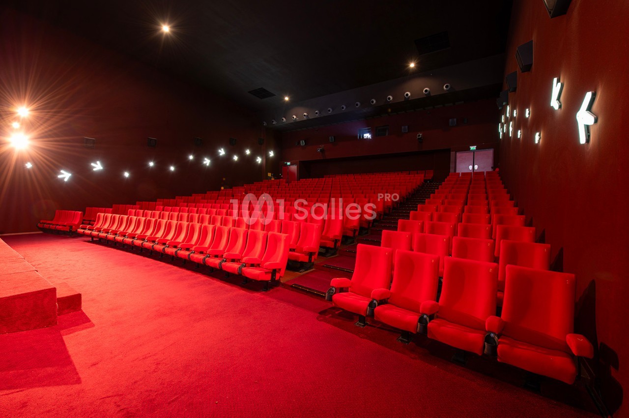 Salle de cinéma vide avec des rangées de fauteuils rouges et un éclairage tamisé.