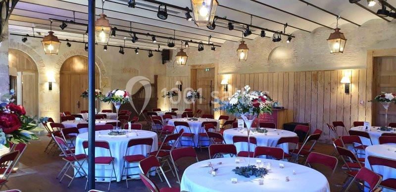 Salle de réception décorée avec des tables rondes, nappes blanches, chaises rouges et arrangements floraux.