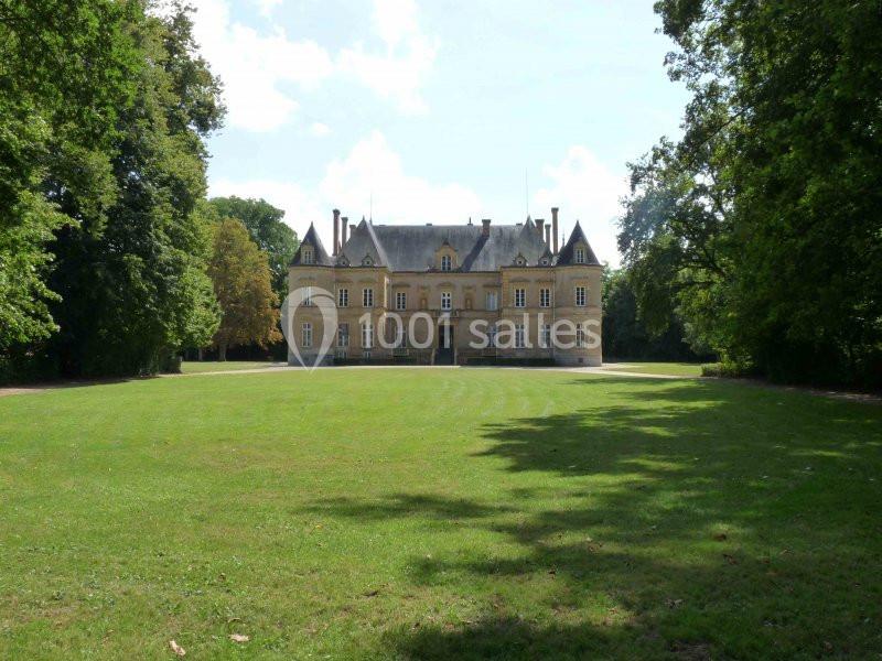 Façade d'un château entouré de pelouses et d'arbres, sous un ciel partiellement nuageux.