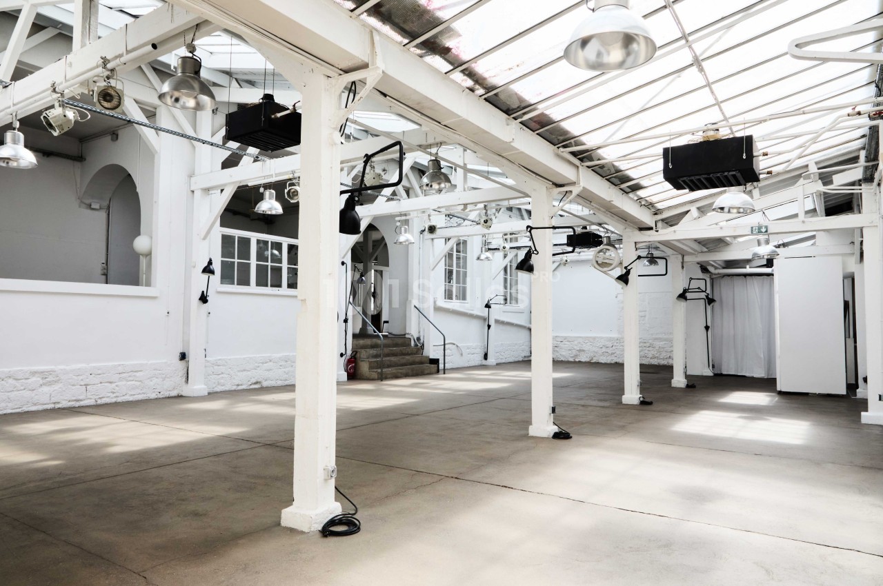 Espace intérieur lumineux avec structure métallique blanche, sol en béton et toit en verrière.