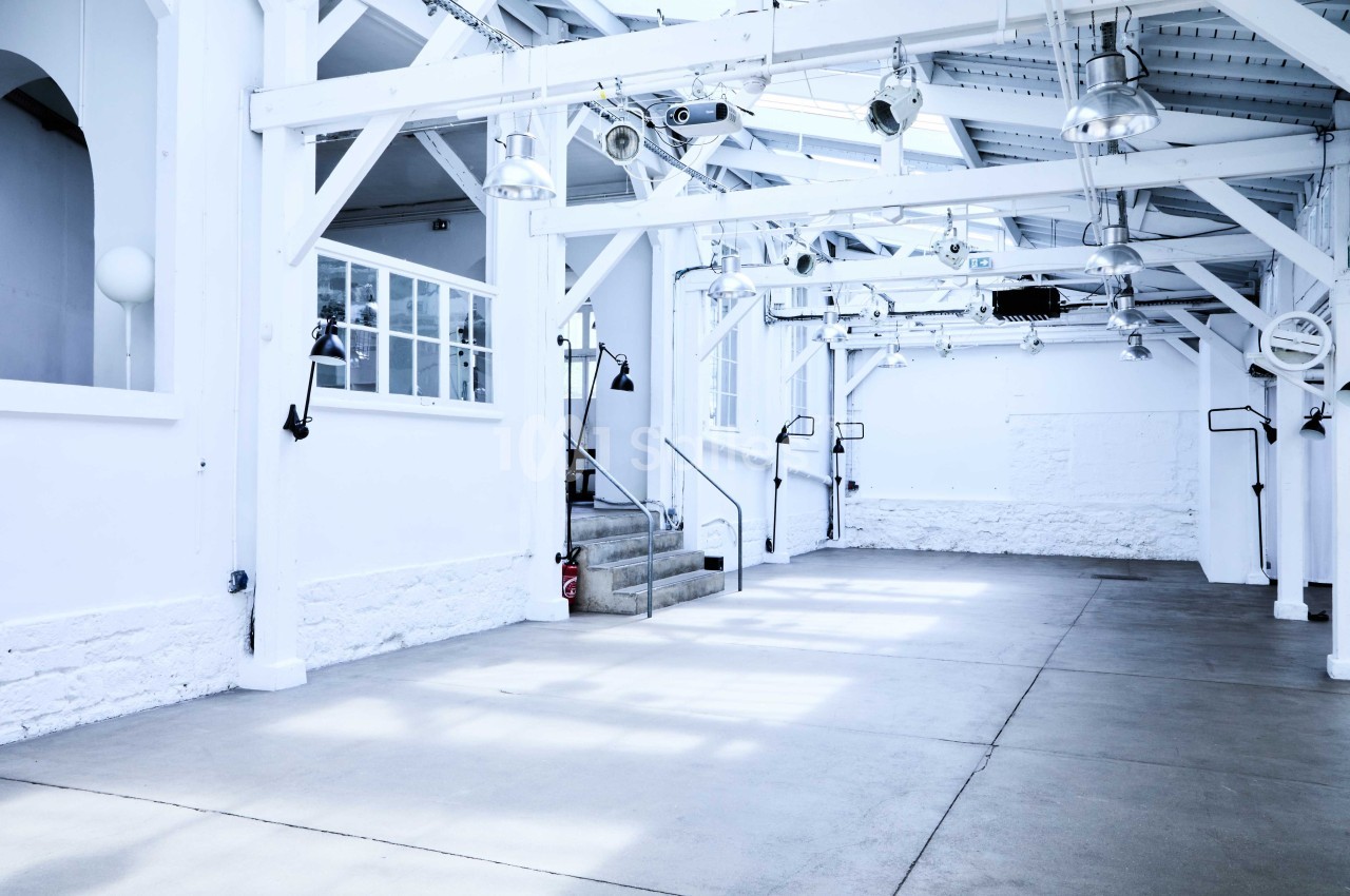 Intérieur d'un grand espace lumineux avec des poutres blanches, des fenêtres et des lampes suspendues.