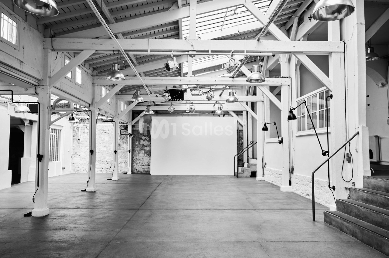 Intérieur d'un espace industriel rénové avec poutres apparentes, murs blancs et sol en béton poli.