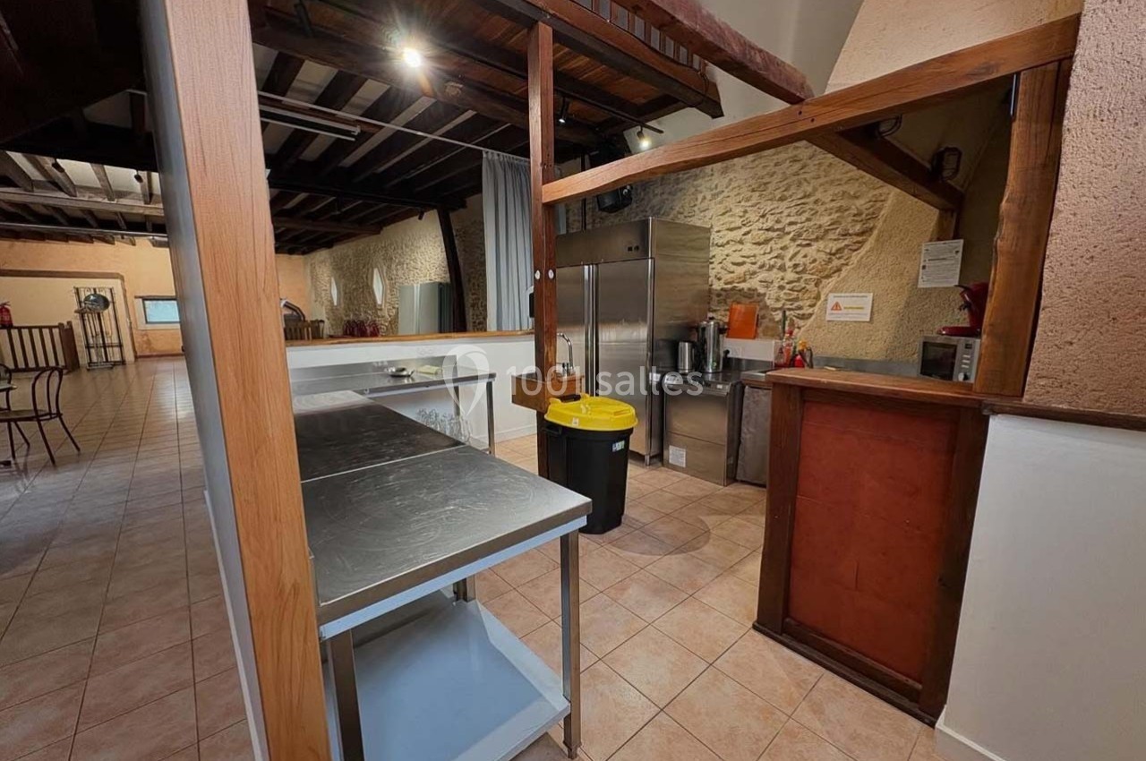 Cuisine spacieuse avec plans de travail en inox, réfrigérateurs, poubelle jaune et murs en pierre apparente.