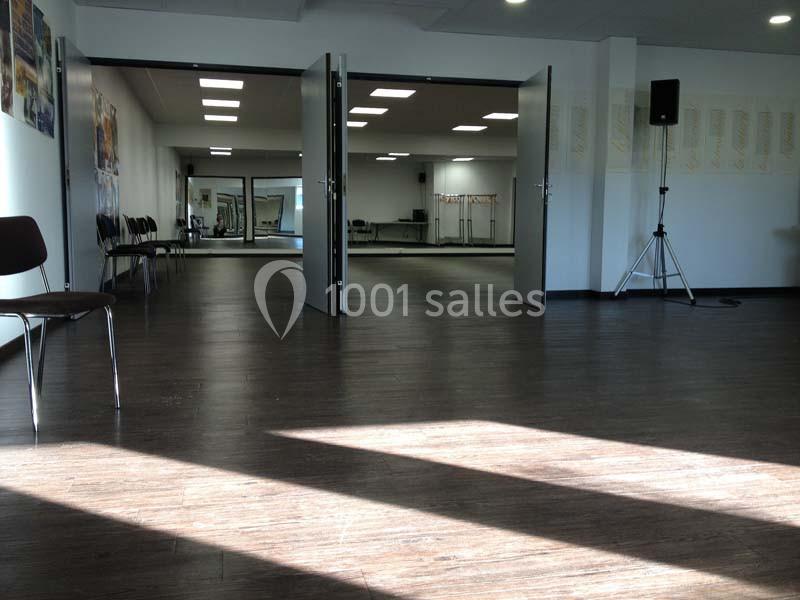 Salle spacieuse avec parquet sombre, chaises alignées sur les côtés et miroirs couvrant un mur au fond.