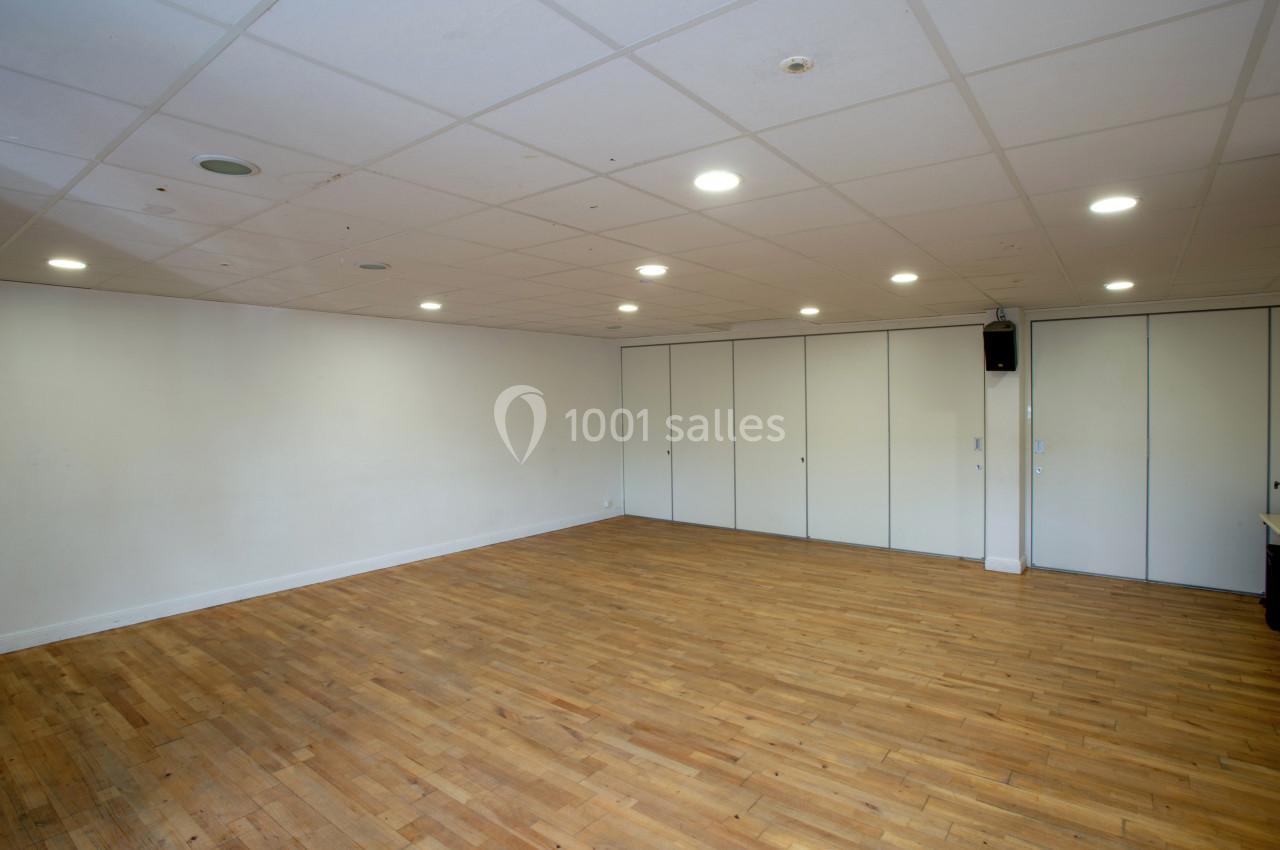 Salle vide avec parquet en bois clair, murs blancs, plafond à dalles et éclairage encastré.