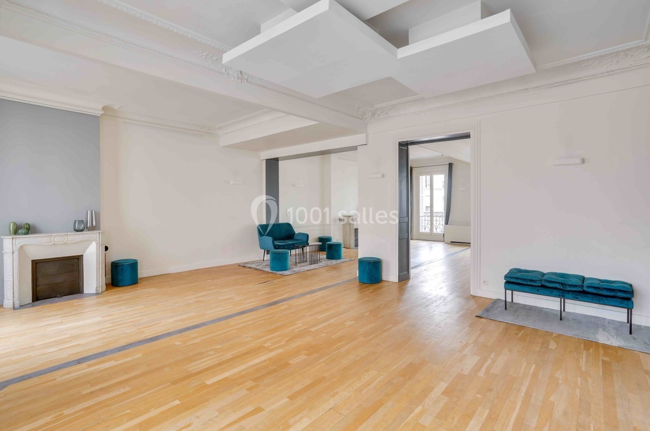 Salon lumineux avec parquet en bois clair, cheminée, fauteuils bleus et moulures au plafond.