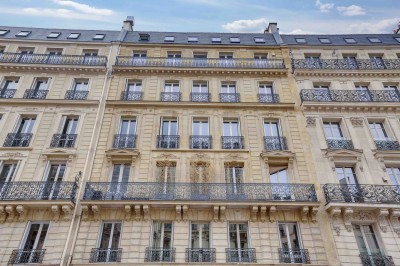 Façade d'un immeuble haussmannien avec balcons en fer forgé et fenêtres alignées sur plusieurs étages.