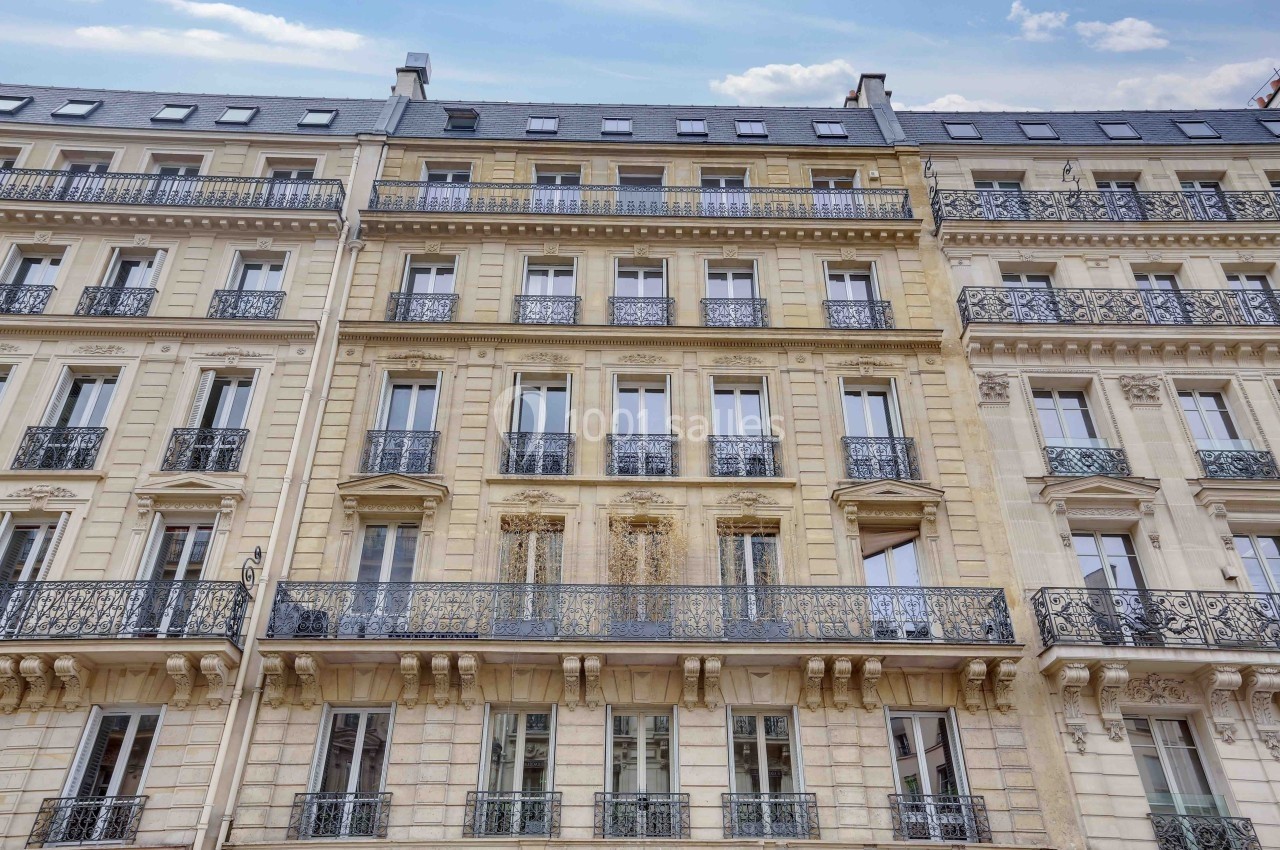 Façade d'un immeuble haussmannien avec balcons en fer forgé et fenêtres alignées sur plusieurs étages.