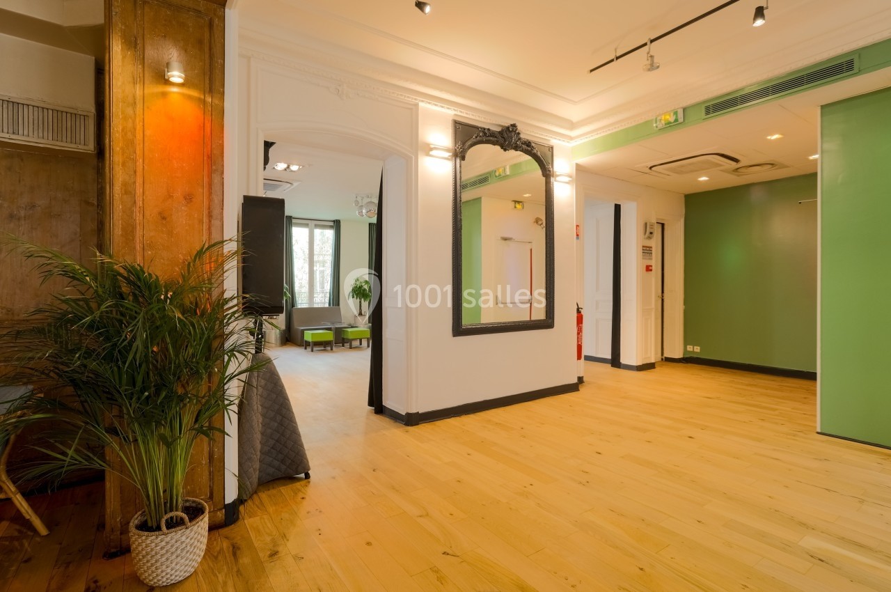 Intérieur lumineux avec parquet, murs blancs, miroir encadré noir, plantes et portes vertes.