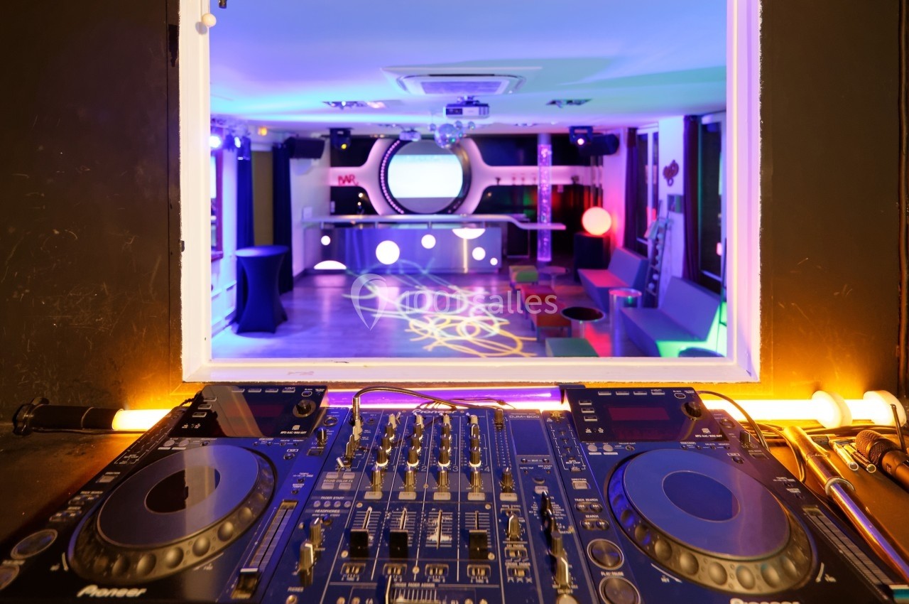 Vue d'une cabine de DJ avec platines en premier plan et une salle colorée éclairée en arrière-plan.