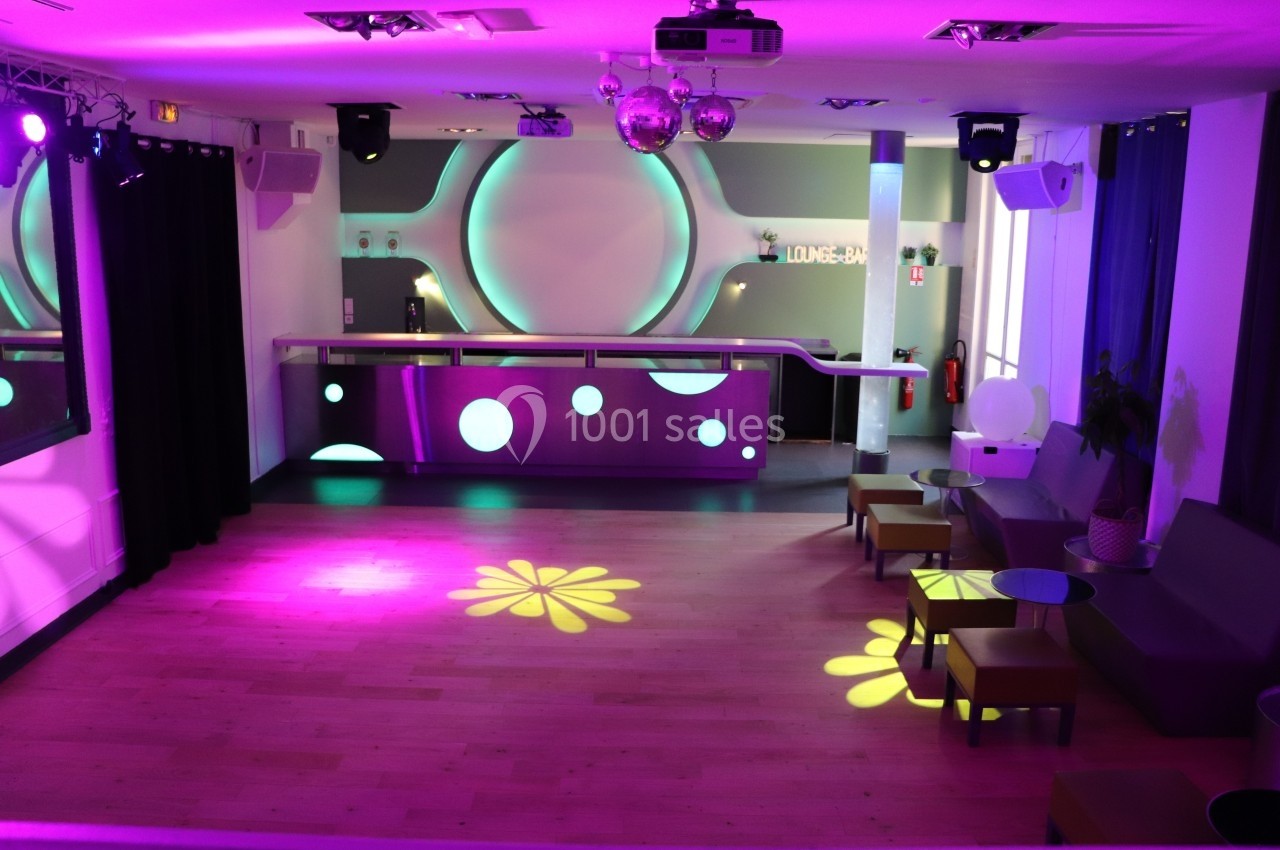 Salle de réception moderne avec bar éclairé, parquet en bois clair et jeux de lumières colorées au sol.