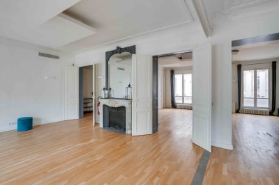 Salon lumineux avec parquet en bois clair, cheminée, fauteuils bleus et moulures au plafond.