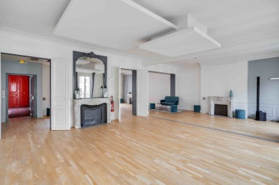Salon lumineux avec parquet en bois clair, cheminée, fauteuils bleus et moulures au plafond.