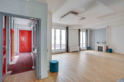Salon lumineux avec parquet en bois clair, cheminée, fauteuils bleus et moulures au plafond.